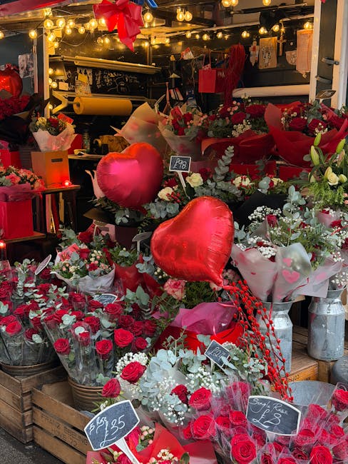 A vibrant display of floral arrangements at Sheen Lane East Sheen featuring red roses, white flowers, and green foliage, all wrapped in paper and placed in wooden crates. Prominent among the flowers a